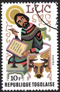 Ein Mann mit einem Heiligenschein und ienem langen Gewannt hat einen Stift in der einen Hand und in der Anderen ein Papier, das er beschrieben h at. Unten rechts ist ein Stier zu sehen