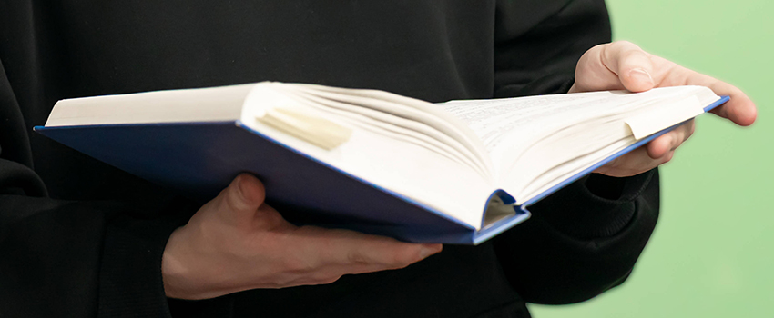 Ein Buch mit Blauem Einband in den Händen einer Person