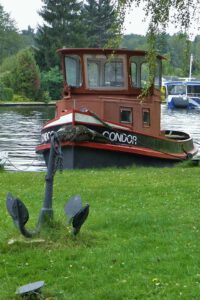 Ein Anker auf einer Wiese mit einem Fischerboot im Hintergrund