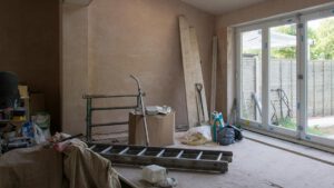 Eine Baustelle mit einer Leiter und Werkzeug in einem Haus mit Terassenfenstern im Hintergrund