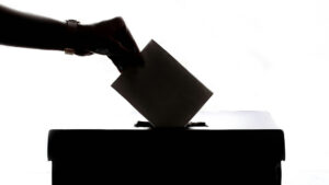 Silhouette einer Hand, die einen Wahlumschlag in eine Wahlurne steckt